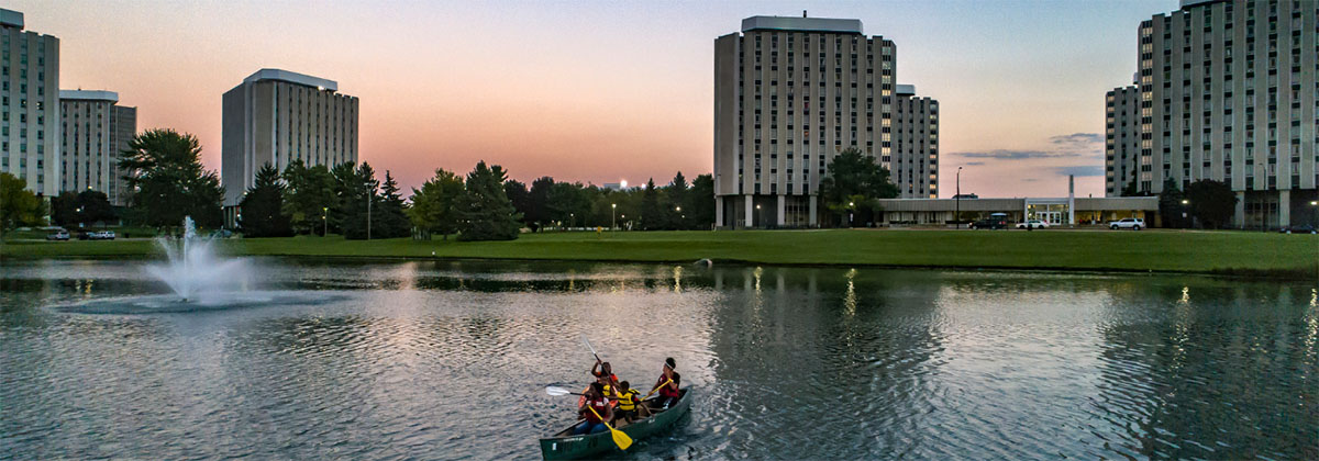 Student canoe on the west lagoon with the residence halls in the background.
